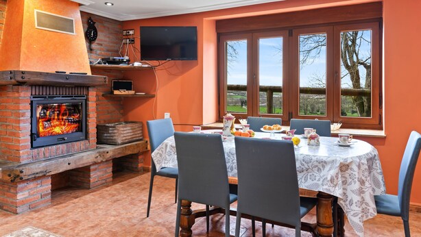 Un coin repas agrémenté d’une cheminée en briques, d’une table dressée pour quatre personnes et d’une fenêtre donnant sur les arbres.