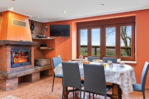 Un comedor con chimenea de ladrillo, una mesa dispuesta para cuatro personas y una ventana con vistas a árboles.