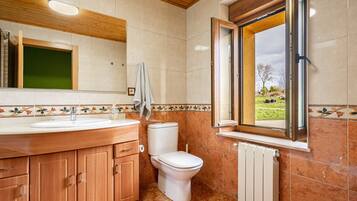 Een badkamer met een houten wastafelmeubel, een toilet, een raam met uitzicht en een betegelde spatwand.