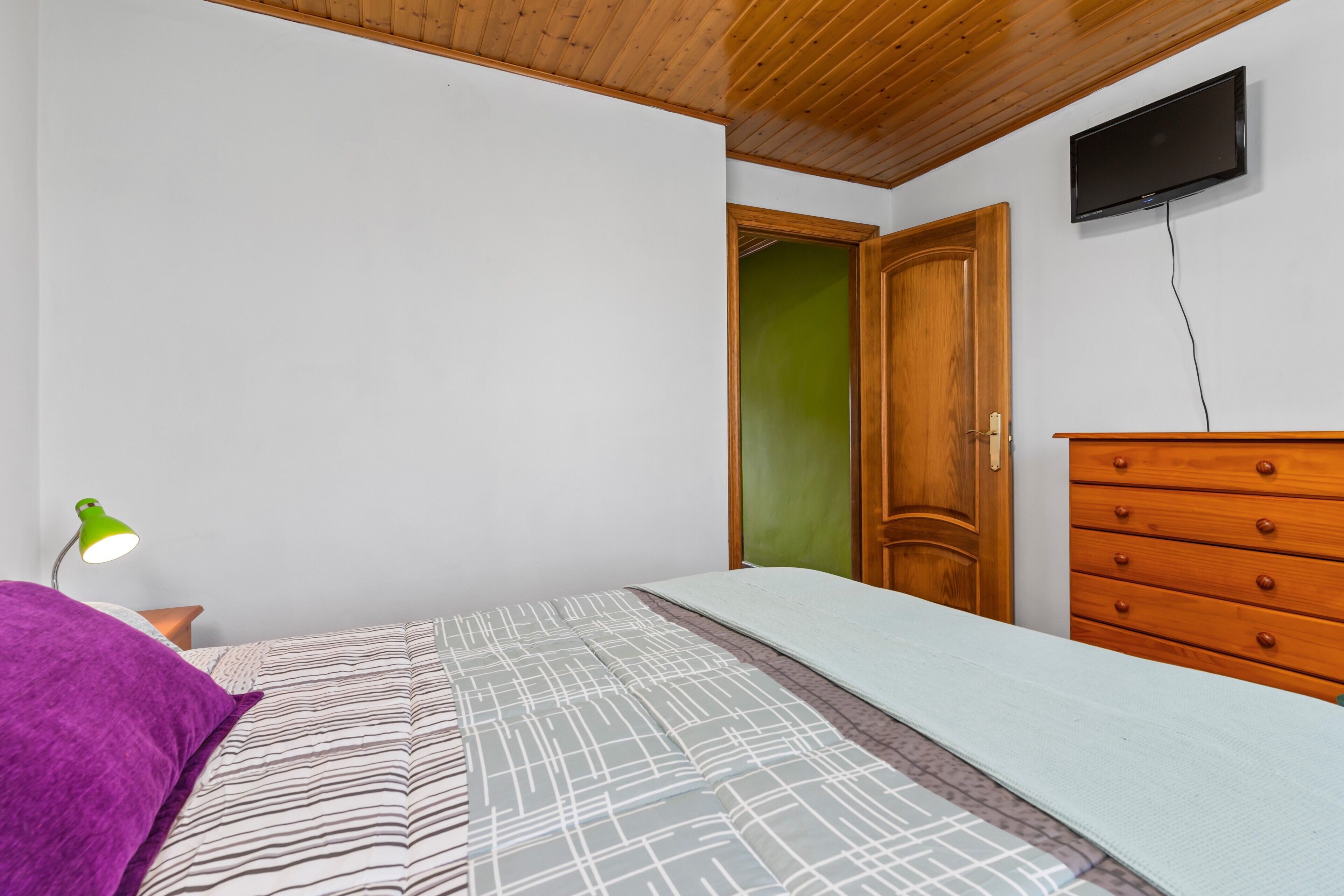 Un dormitorio con una cama, un aparador, un televisor y una puerta verde.