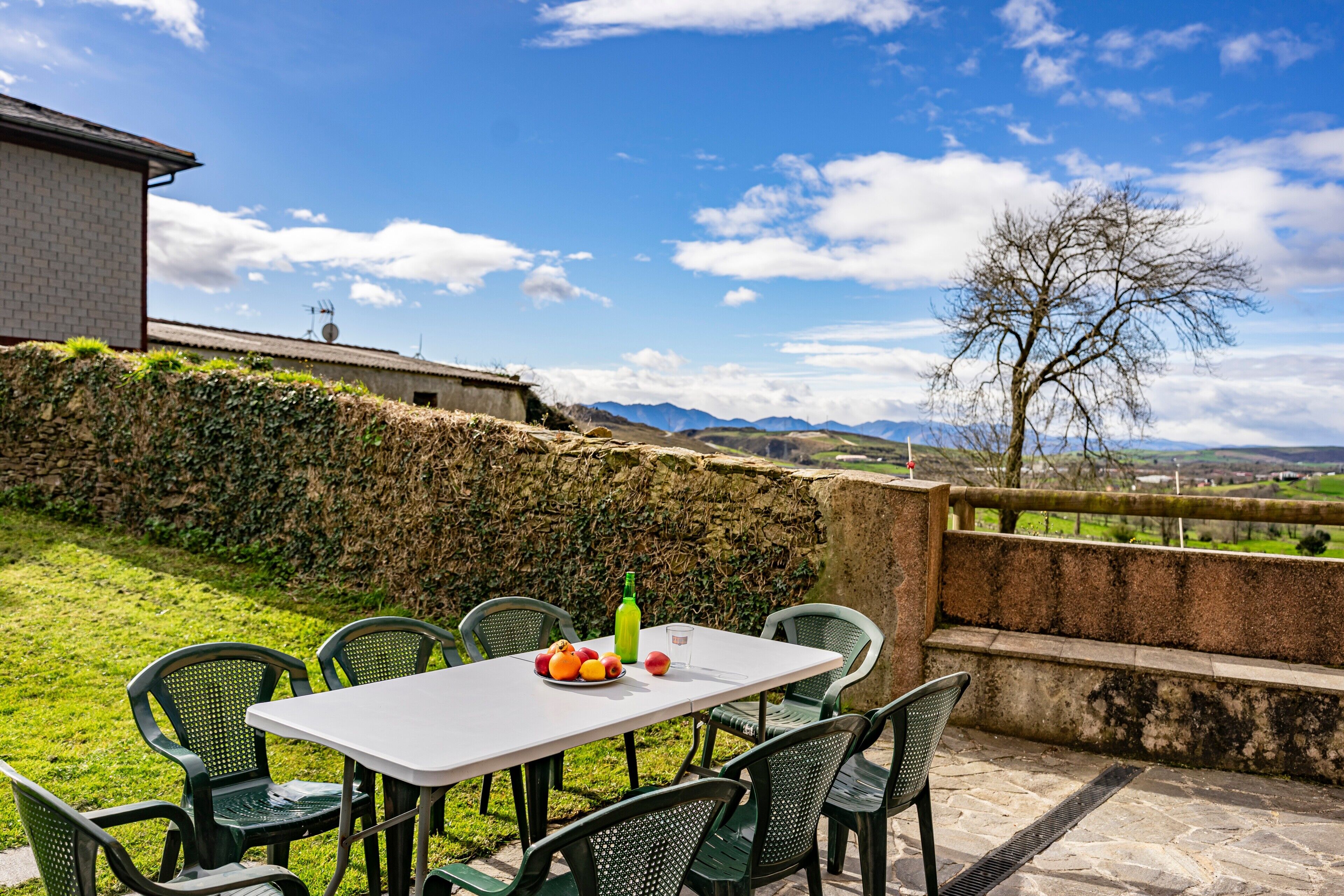 Un espacio de comedor al aire libre con una mesa, sillas, una botella de aceite de oliva y un plato de fruta.