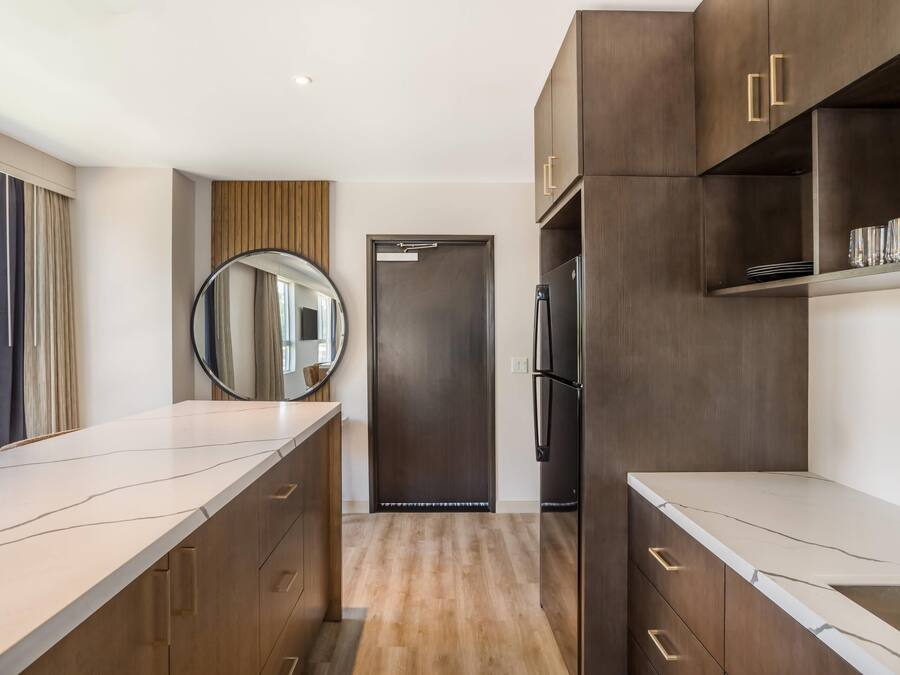 Cocina moderna con encimera de mármol, armarios de madera, refrigerador integrado y un espejo grande.