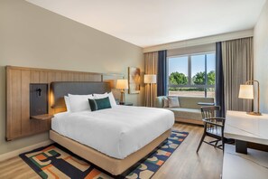 A hotel room with a large bed, a desk, a chair, a sofa, and a view of the outdoors.