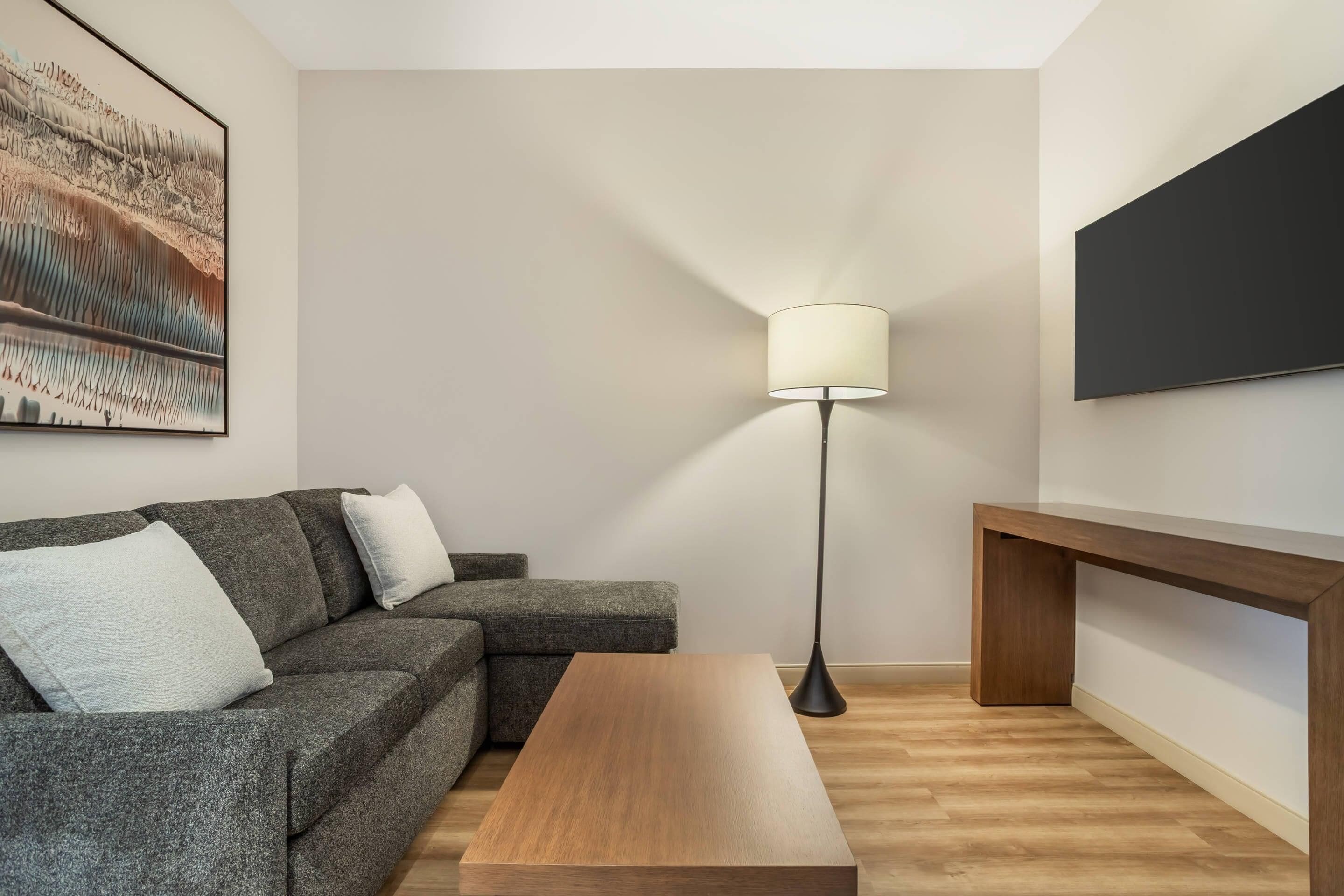 Un salon moderne avec un canapé gris, une table basse en bois, une lampe sur pied et un grand tableau accroché au mur.