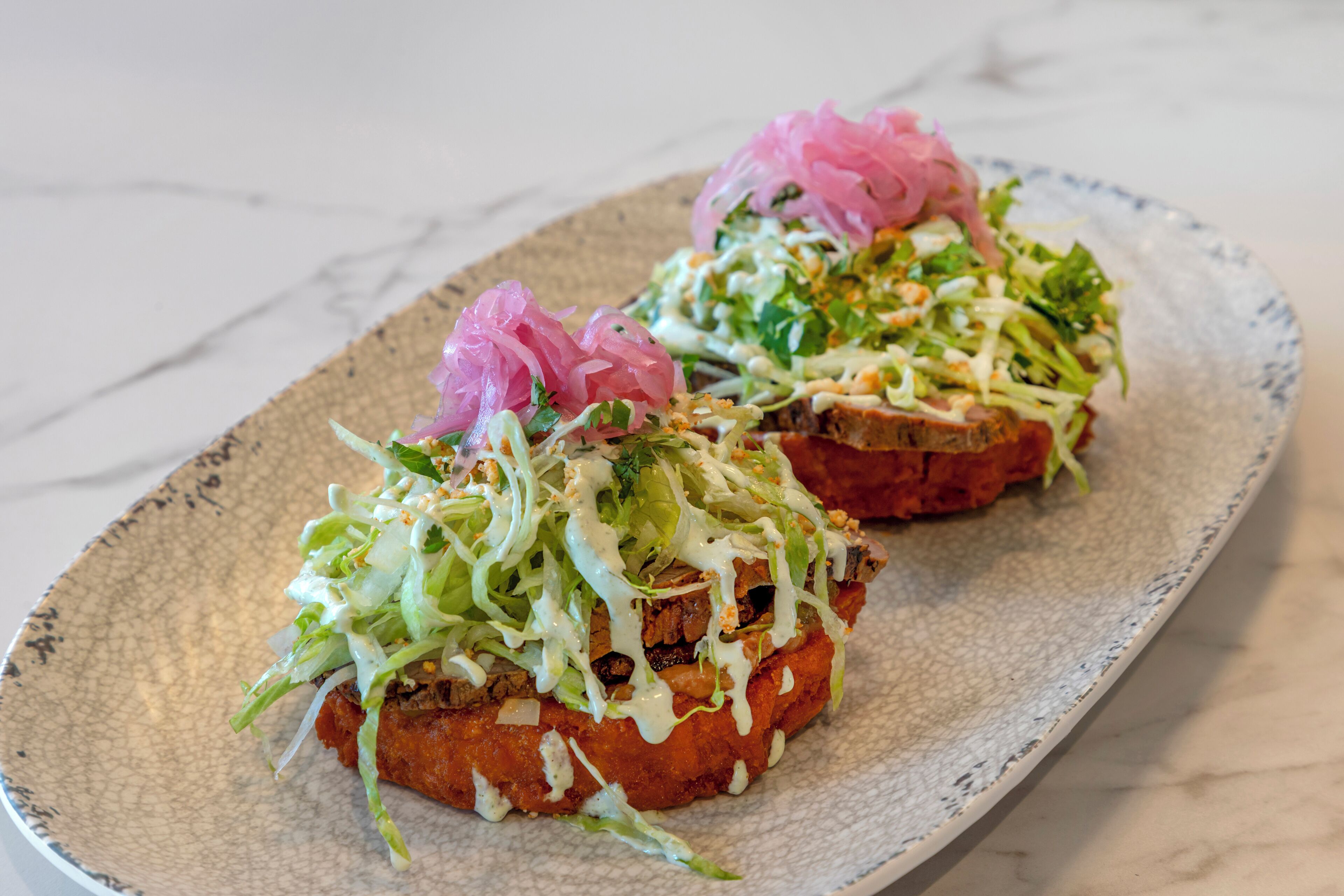 Two sandwiches on a ceramic plate with a textured surface.