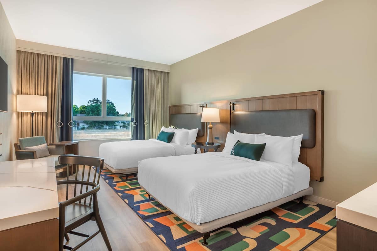Une chambre d’hôtel avec deux lits, un bureau et une vue sur l’extérieur.