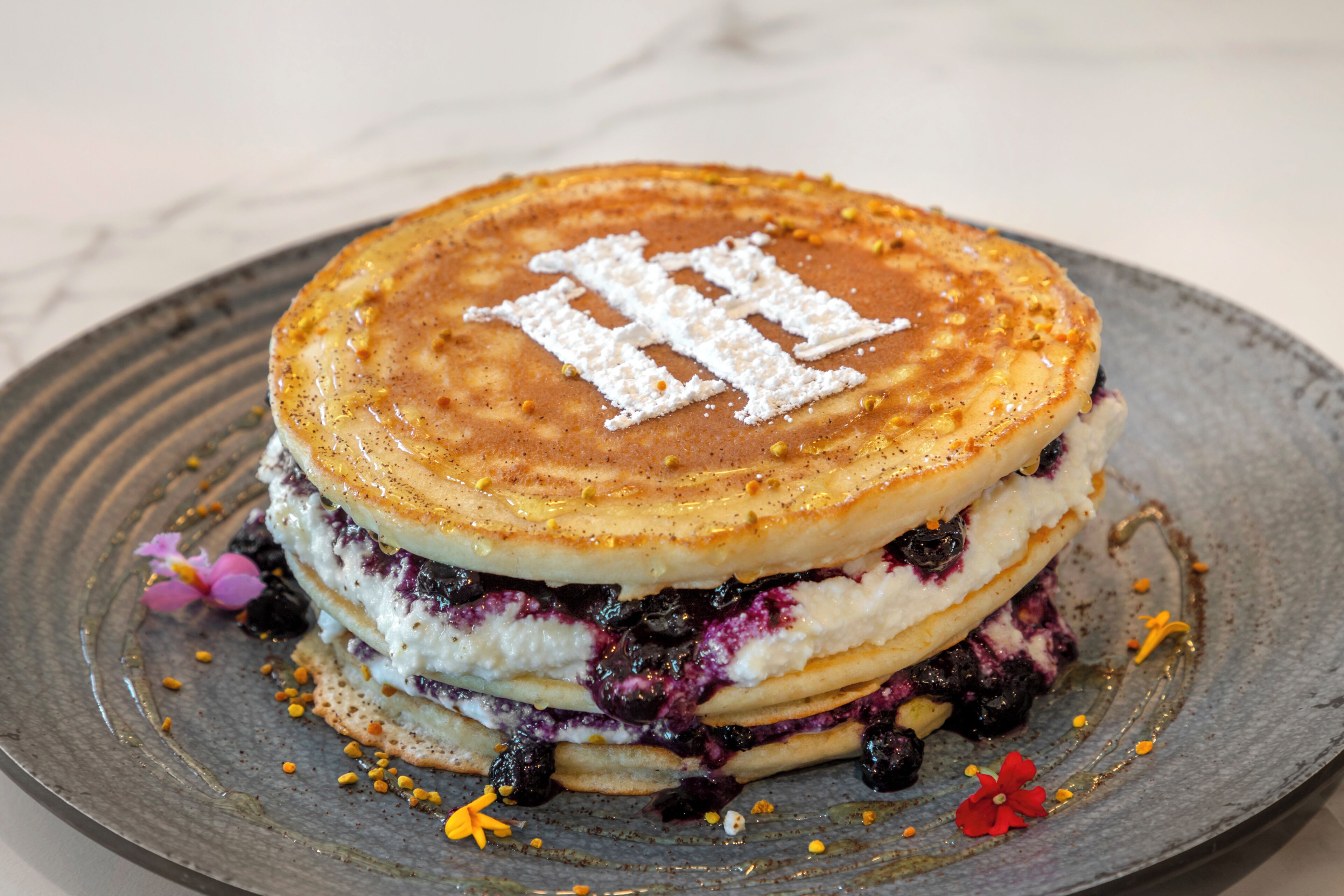 En hög med pannkakor, blåbär och florsocker på en tallrik.