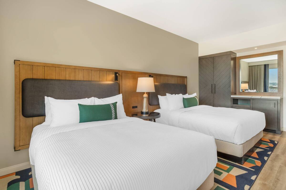 Une chambre d’hôtel avec deux lits, une table de chevet, une lampe, un miroir et une vue sur la ville.