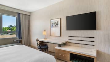 Hotelkamer met een groot bed, een bureau met stoel, een aan de muur bevestigde televisie en een raam met gordijnen.