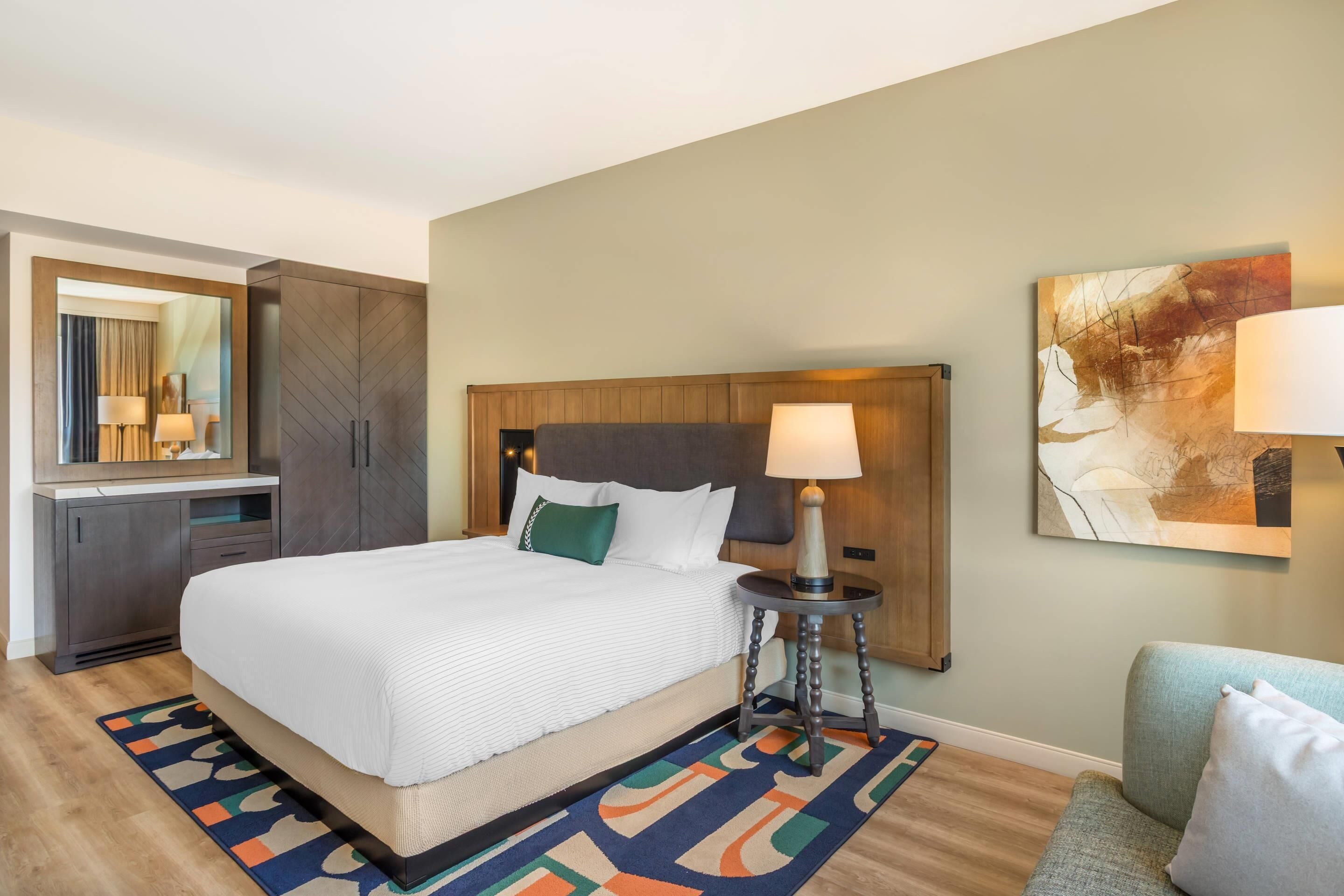 Une chambre d’hôtel comprenant un lit, une table de chevet, une lampe, une œuvre d’art et un coin salon.