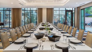 Una larga mesa de comedor dispuesta para una comida formal, con sillas a ambos lados, ventanas amplias y vistas al exterior.