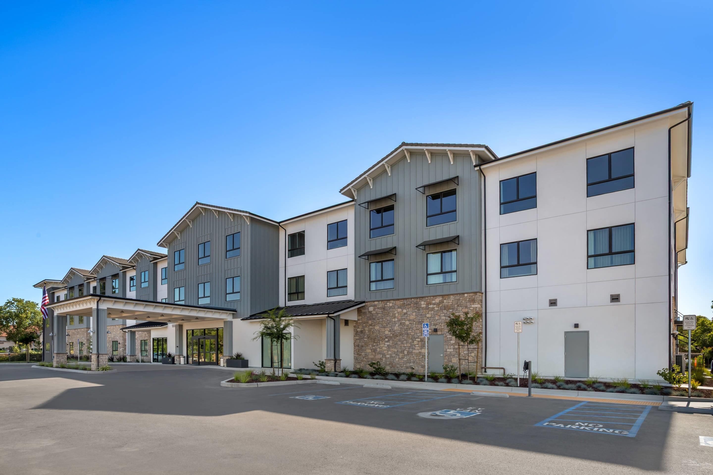 A multi-story hotel with a modern design, featuring a covered entrance and a parking area with handicapped accessibility.