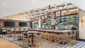 Zona de bar con diversas opciones de asientos, una barra con una variedad de botellas y un diseño moderno en el techo.