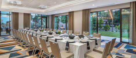 Un salón de conferencias con una larga mesa dispuesta para una reunión, ventanas amplias y vistas al exterior.