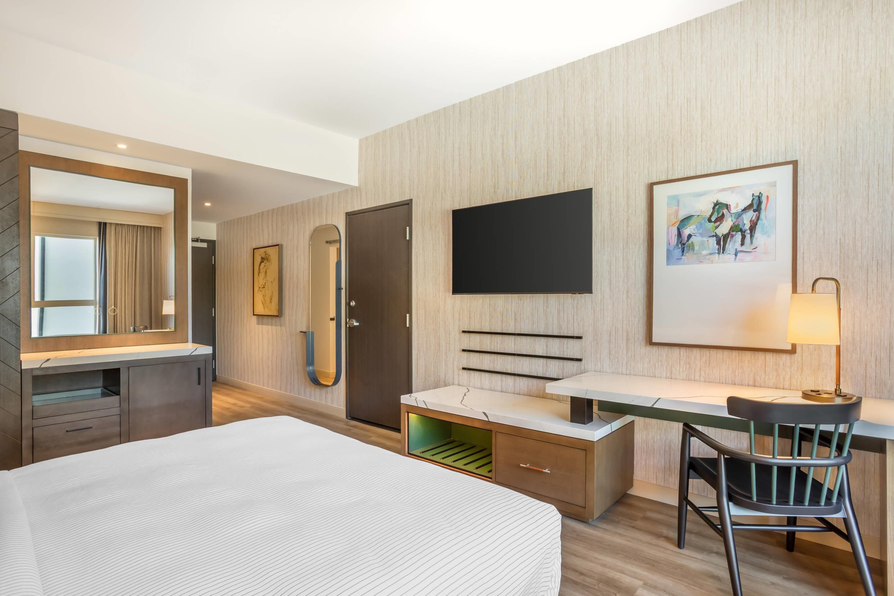 Une chambre d’hôtel moderne, équipée d’un lit, d’un bureau, d’une chaise, d’une télévision et d’un tableau au mur.