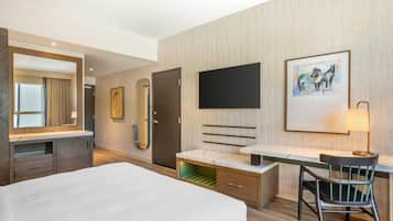 Une chambre d’hôtel moderne, équipée d’un lit, d’un bureau, d’une chaise, d’une télévision et d’un tableau au mur.