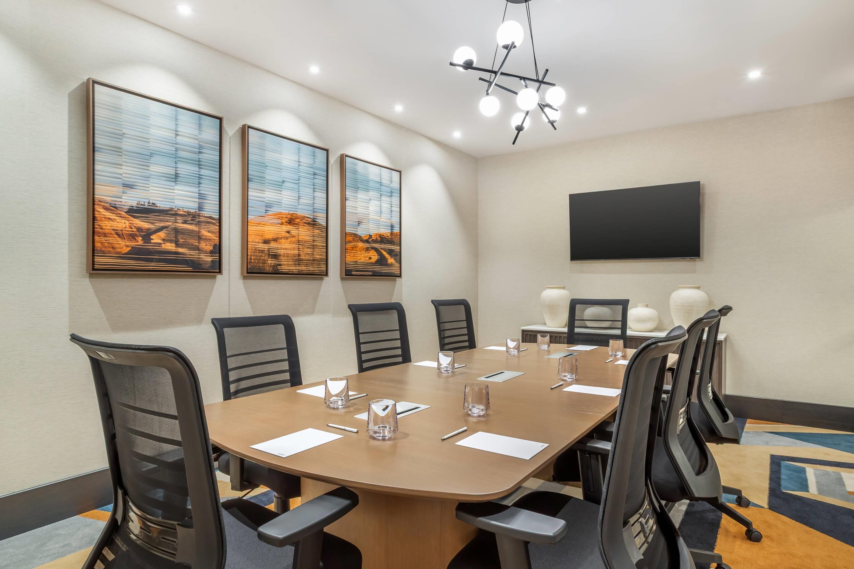A conference room with a long table, six chairs, and three large landscape paintings.