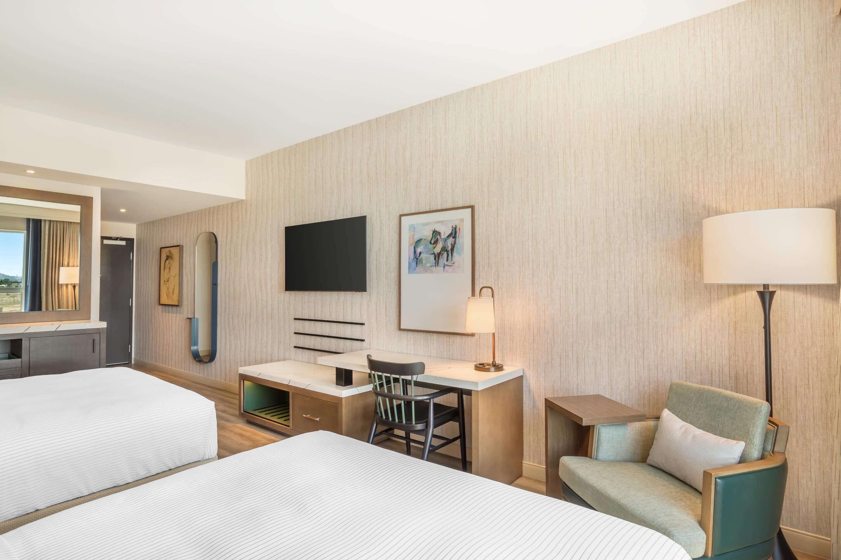 Een hotelkamer met twee bedden, een bureau, een stoel, een televisie en een lamp.