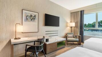 A modern hotel room with a large bed, a desk with a chair, a television, and a window with a view of the outdoors.