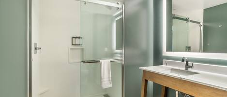 A modern bathroom with a glass shower enclosure, a wooden vanity, and a large mirror.