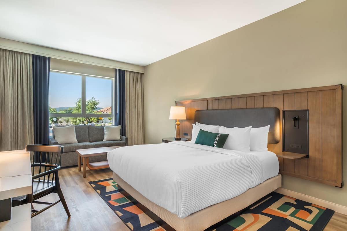 Une chambre d’hôtel avec un grand lit, un bureau, une chaise, un canapé et une fenêtre donnant sur un beau paysage.