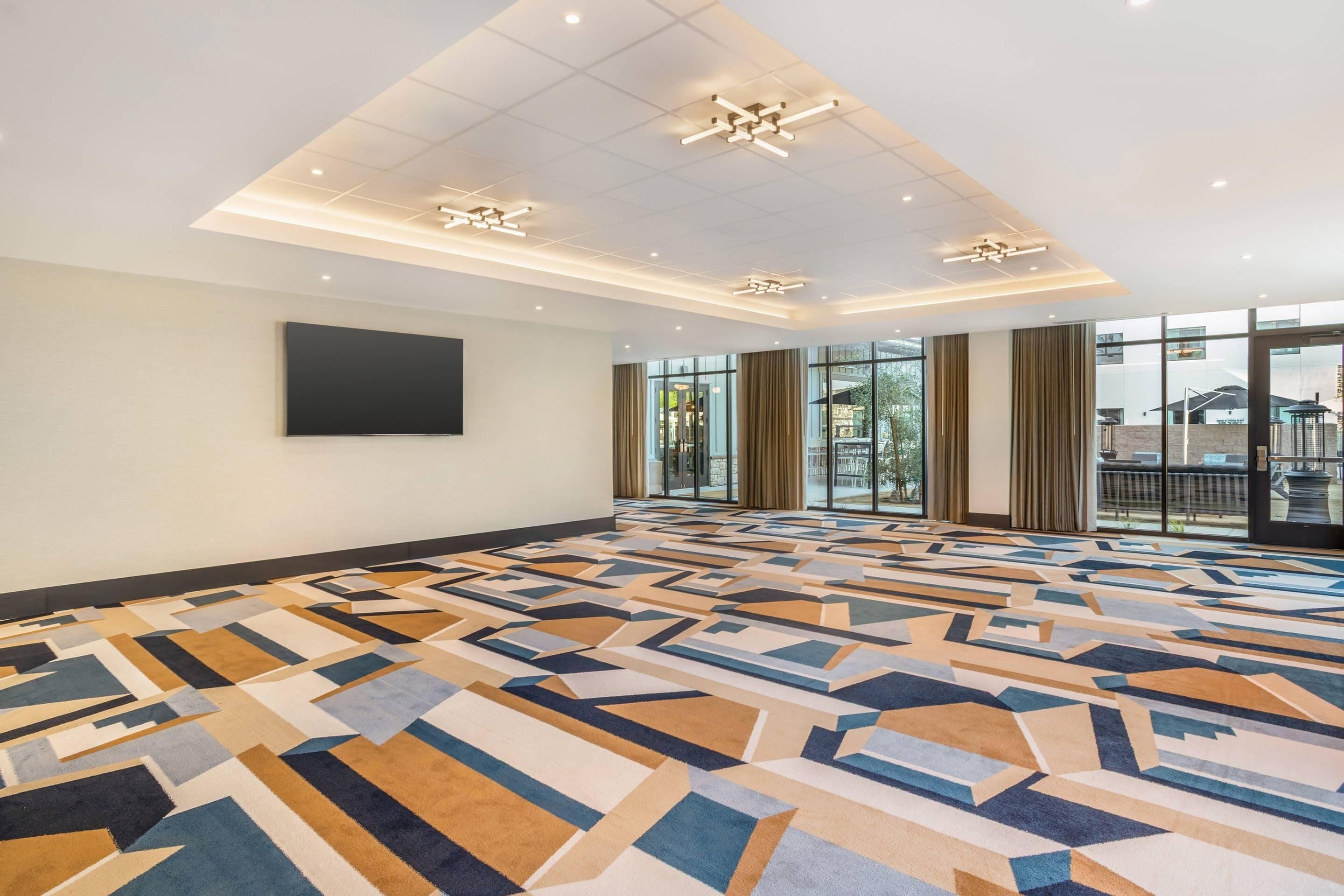 A spacious room with a patterned carpet, large windows, and ceiling lights.