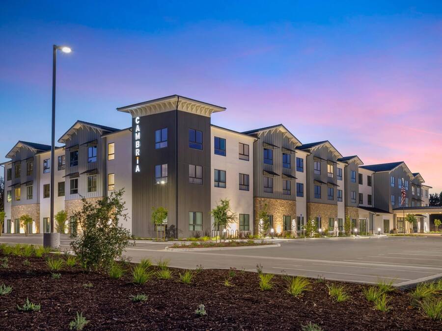 Un hotel de varios pisos con un diseño moderno, que presenta un patio central con jardines y una zona de estacionamiento.