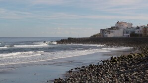 A coastal scene with a rocky beach, waves, and buildings in the background.