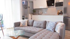 A modern living room with a sofa, a glass coffee table, and a kitchen area with appliances.