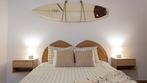 A bed with a checkered bedspread, two bedside tables with lamps, and a surfboard decoration on the wall.