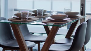 A dining table with chairs, a glass top, and a hanging light fixture.