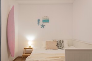 A bedroom with a bed, a nightstand, a lamp, a surfboard, and a sign on the wall.