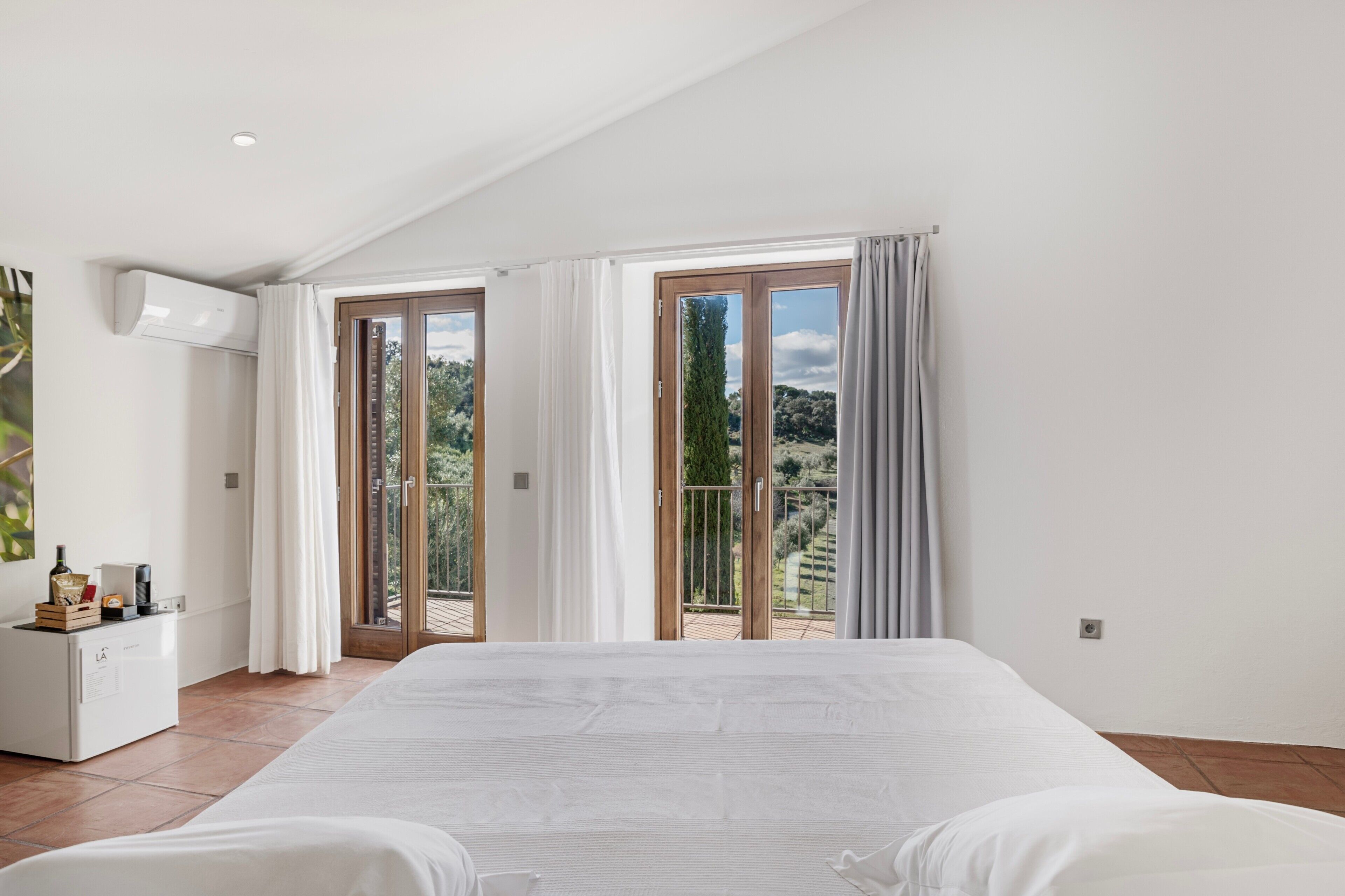 Un dormitorio con una cama grande, un minibar y vistas al exterior a través de un ventanal corredero.