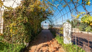 Un sentier agrémenté d’une arche métallique, d’une cloche et offrant une vue sur un bâtiment situé au loin.
