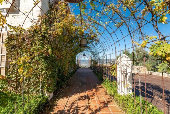 A pathway with a metal archway, a bell, and a view of a distant building.