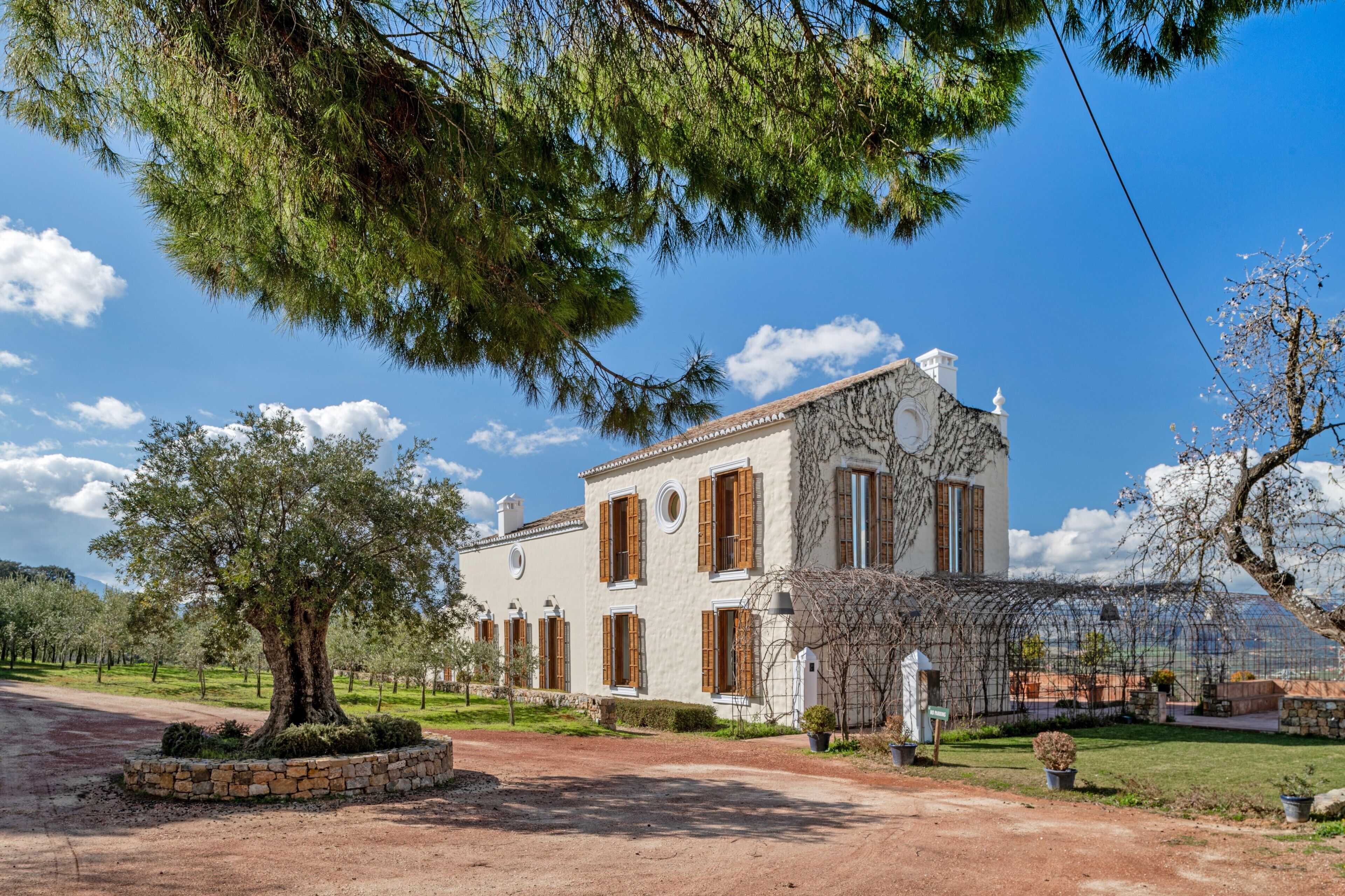 Un edificio de dos pisos con fachada de piedra, contraventanas de madera y un jardín con un árbol grande.