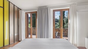 Une chambre avec un grand lit, des portes-fenêtres coulissantes donnant sur un balcon et un mur jaune.
