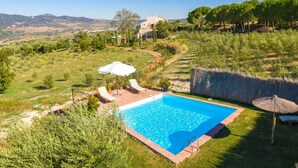 Une piscine entourée de chaises longues et de parasols, elle-même bordée d’un jardin aménagé et offrant une vue sur des collines lointaines.