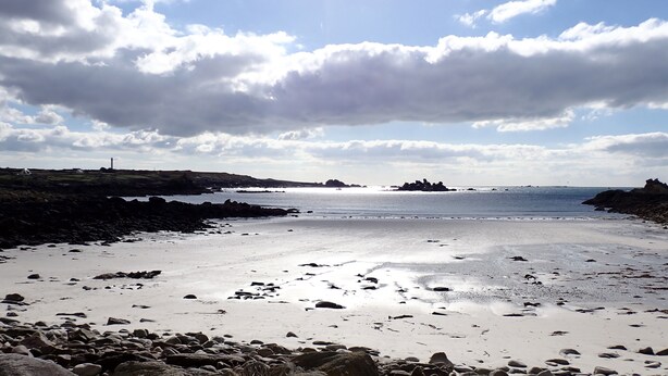A coastal beach with rocky terrain and a lighthouse in the distance.