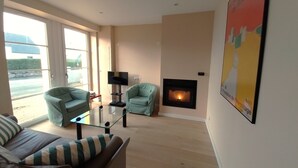 A living room with a fireplace, two armchairs, a glass coffee table, and a television.