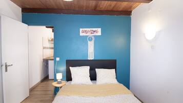 A bedroom with a bed, a nightstand, a wall-mounted light, and a door leading to another room.