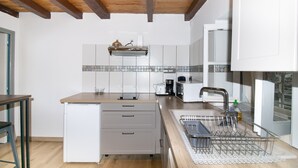 Eine Küche mit Holzbalkendecke, weißen Schränken, einem kleinen Kühlschrank, einer Kaffeemaschine und einem Geschirrgestell.