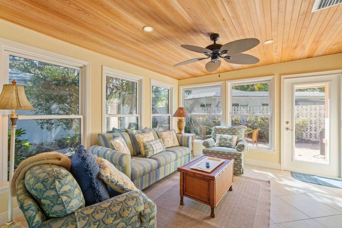 A spacious living room with a ceiling fan, large windows, and a view of the outdoors.