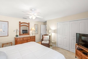 A hotel room with a large bed, a wooden dresser, a television on a stand, a ceiling fan, and a wardrobe.