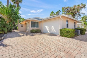 A single-story house with a garage, paved driveway, and surrounding greenery. - Huge Villa! Sunroom, Pool, Near Crescent Beach! (Siesta Key)