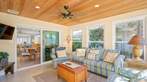 A spacious living room with a wooden ceiling, a large window, a sofa set, a coffee table, and a lamp.