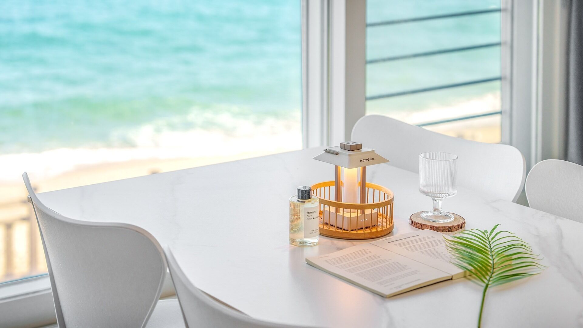 Une table blanche, ornée d’une bougie, d’une bouteille et d’un menu, donnant sur une plage.