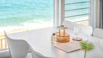Una mesa blanca con una vela, una botella y un menú, con vistas a una playa.