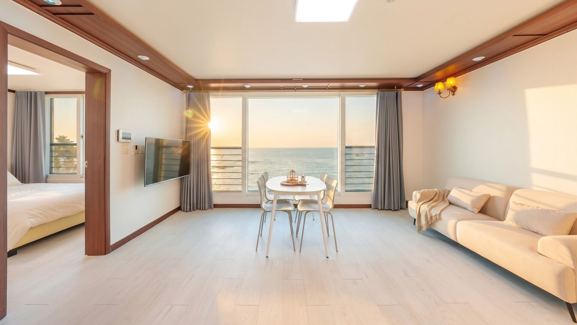 Una habitación de hotel moderna con un gran ventanal que ofrece vistas al mar, una zona de comedor con mesa y sillas, un sofá y un televisor de pantalla plana montado en la pared.