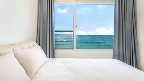 Een hotelkamer met een bed, een raam met uitzicht op de oceaan en grijze gordijnen.
